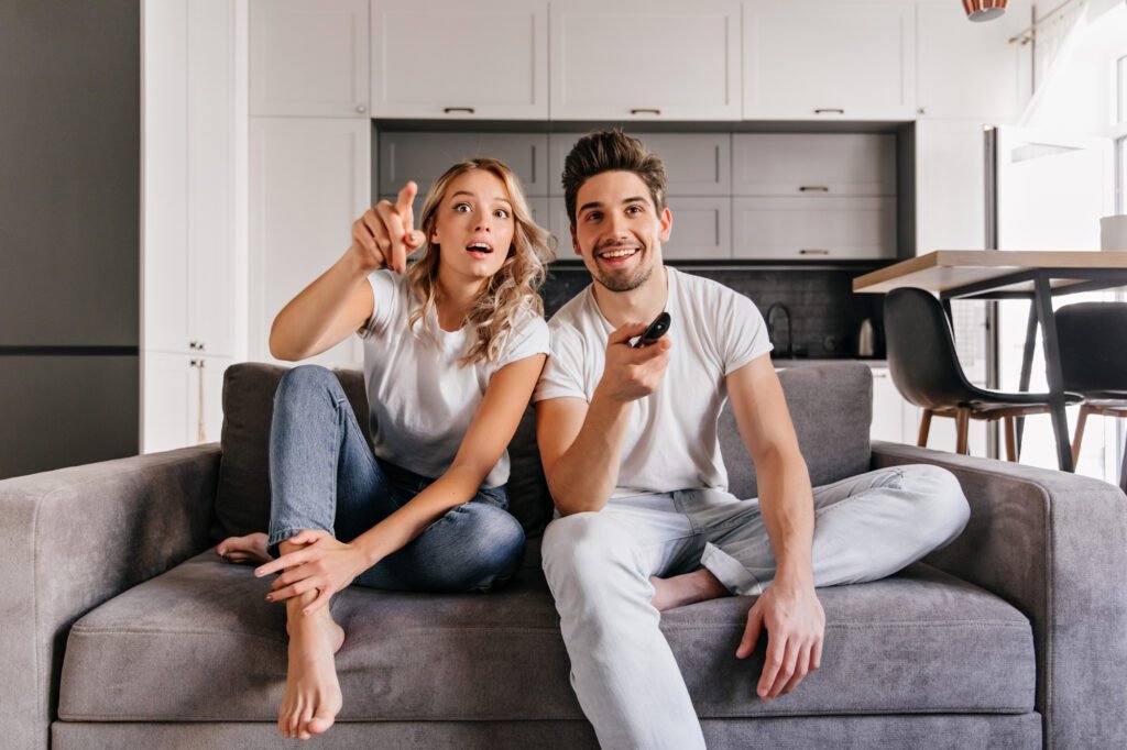 curious couple sitting grey sofa indoor portrait man woman watch tv